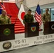 A military press conference is being held at Camp Asaka, Japan, for exercise Yama Sakura 91 (YS-91). Three military officers — appearing to represent Australia, Japan, and the United States — stand at separate podiums in front of their respective national flags. A banner in English and Japanese identifies the event as the YS-91 Press Conference at Camp Asaka.