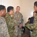 The image shows a group of military personnel from what appear to be two different armed forces engaged in a discussion or briefing in an indoor setting. U.S. Army soldiers wearing OCP (Operational Camouflage Pattern) uniforms are interacting with personnel wearing Japanese Ground Self-Defense Force (JGSDF) camouflage uniforms. The setting suggests a joint military exercise, coordination meeting, or liaison activity.