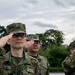 Three military personnel in Japanese Ground Self-Defense Force (JGSDF) camouflage uniforms are performing a formal salute. The foreground soldier has a visible name tag reading 'N. BETSUI' and wears glasses. The scene appears to be an outdoor military ceremony or formation.