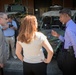 Four individuals are gathered in an outdoor area in front of military-style tactical vehicles, likely at a defense facility or military installation. Three people appear to be engaged in a professional discussion, while a fourth person photographs the scene in the background. The setting and vehicles suggest an official visit, demonstration, or briefing related to military equipment.