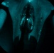 The image appears to be captured through a night vision or image intensifier device, producing a characteristic circular green-teal tinted view. The scene shows what appears to be the interior of a large military aircraft, likely viewed through the open rear cargo ramp or door, with at least one figure visible inside. The low-light imaging technology creates a grainy, monochromatic teal appearance typical of night vision optics.