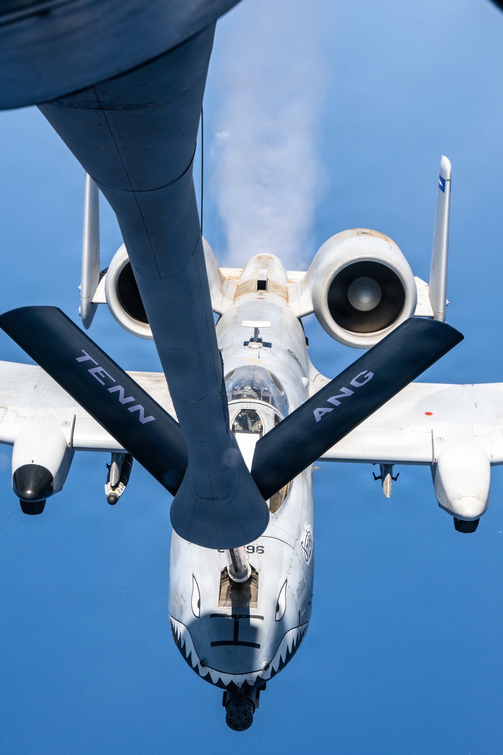 An A-10 Thunderbolt II (Warthog) attack aircraft is receiving aerial refueling from a tanker aircraft, photographed from the boom operator's position looking down at the receiver aircraft. The A-10 bears 'TENN ANG' markings on its wings, indicating it belongs to the Tennessee Air National Guard. The aircraft displays the characteristic shark mouth nose art and the refueling boom is visibly connected to the aircraft's receptacle.