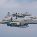 Two U.S. Air Force A-10 Thunderbolt II (Warthog) aircraft flying in close formation against an overcast sky. Both aircraft display shark mouth nose art and carry underwing ordnance/stores. The tail codes and markings indicate they belong to the same unit, with 'FT' tail codes and red unit designator badges visible.