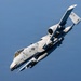 A U.S. Air Force A-10 Thunderbolt II (Warthog) attack aircraft is captured in a steep banking maneuver against a clear blue sky, with what appears to be a body of water visible below. The aircraft displays the iconic shark mouth nose art and carries visible ordnance/weapons on its wing pylons. The image is a high-quality aerial photograph likely taken from another aircraft.