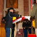 A military ceremony is taking place inside what appears to be the Indiana War Memorial, as indicated by the podium signage reading 'Honoring Hoosier Veterans' and 'War Memorial.' A soldier in dress uniform and cavalry Stetson hat is unfurling or presenting a unit guidon banner reading 'Squadron, 152nd Cavalry.' Several uniformed soldiers stand at attention in the background as part of a formal color guard or activation/inactivation ceremony.