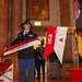 A U.S. Army soldier in dress uniform and cavalry black Stetson hat is holding an organizational streamer or guidon banner reading 'A Troop, 1st Squadron, 152nd Cavalry' during a formal military ceremony. The event appears to be taking place inside a war memorial building, with marble columns, an American flag, and military unit colors visible. Additional soldiers and civilians are present in the background.
