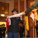 A formal U.S. Army military ceremony is taking place in an ornate indoor venue, likely a government or historic building. A soldier wearing a cavalry black Stetson hat and dress uniform is receiving or presenting a unit guidon/flag, with the text 'B TROOP' and 'CAVALRY' visible on the furled flag. Multiple soldiers in dress uniforms and cavalry hats are standing at attention in the background near additional unit colors and guidons.