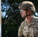 A U.S. Army soldier identified as 'ASHER' by name tape, holding the rank of Staff Sergeant, is photographed in a tactical outdoor setting. He is wearing full combat gear including a multicam uniform, tactical helmet, and protective eyewear. A patch on his right sleeve reads 'COMPETITOR 1', suggesting participation in a military competition or evaluation event.