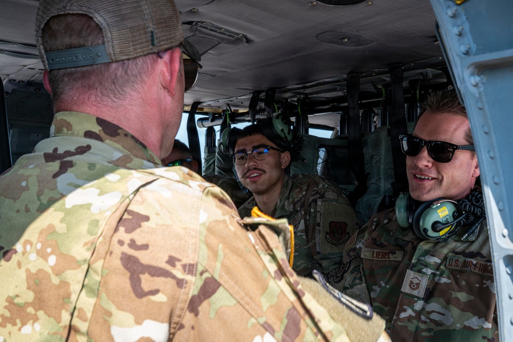 Several U.S. Air Force personnel are gathered inside or at the entrance of a military helicopter, engaged in conversation. At least one individual has a name tape reading 'LIEBEL' and U.S. Air Force insignia is visible on a uniform. The personnel are wearing OCP (Operational Camouflage Pattern) uniforms, with some wearing headsets and sunglasses.