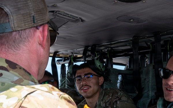 Several U.S. Air Force personnel are gathered inside or at the entrance of a military helicopter, engaged in conversation. At least one individual has a name tape reading 'LIEBEL' and U.S. Air Force insignia is visible on a uniform. The personnel are wearing OCP (Operational Camouflage Pattern) uniforms, with some wearing headsets and sunglasses.