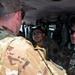 Several U.S. Air Force personnel are gathered inside or at the entrance of a military helicopter, engaged in conversation. At least one individual has a name tape reading 'LIEBEL' and U.S. Air Force insignia is visible on a uniform. The personnel are wearing OCP (Operational Camouflage Pattern) uniforms, with some wearing headsets and sunglasses.