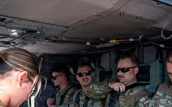 A group of U.S. Air Force personnel in OCP (Operational Camouflage Pattern) uniforms are seated inside a military helicopter, appearing to prepare for or complete a flight. Several personnel are adjusting harnesses and seatbelts, with one female service member standing near the open door. Name tapes and U.S. Air Force branch tapes are visible on multiple individuals.