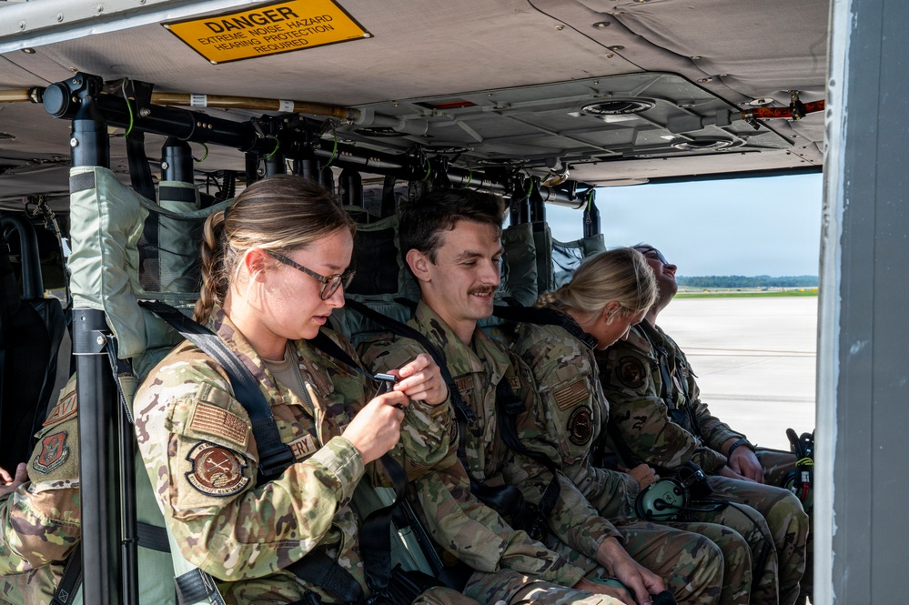 Several U.S. Air Force personnel in OCP (Operational Camouflage Pattern) uniforms are seated inside what appears to be a military helicopter or aircraft cabin. A warning sign reading 'DANGER - EXTREME NOISE HAZARD - HEARING PROTECTION REQUIRED' is visible on the overhead panel. The personnel appear to be preparing for or waiting during a flight operation on an airfield.