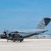 A U.S. Air Force C-17 Globemaster III cargo aircraft assigned to the Air Force Reserve Command (AFRC) Pittsburgh unit, tail number 91189, is parked on a tarmac. In the foreground, a U.S. Army UH-60 Black Hawk helicopter is positioned directly in front of the large transport aircraft. The scene appears to be at a military airfield with hangars visible in the background.