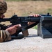 A soldier in MultiCam/OCP camouflage uniform is firing an M4/M16-style rifle from a prone position on a concrete surface at what appears to be a military firing range. A spent brass cartridge casing is visibly ejecting from the weapon's ejection port, captured mid-flight. The soldier's name tape reads 'PENA' and the rifle is rested on a concrete shooting block.