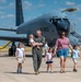 A U.S. Air Force pilot in olive flight suit walks with his family on a flight line tarmac in front of a large military aircraft. The group includes what appears to be a woman and four young children, suggesting a homecoming or family day event at a military air base. The aircraft in the background is identifiable as a KC-135 Stratotanker belonging to the 97th Air Mobility Wing at Altus AFB.