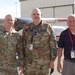 Three men pose in front of a small civilian aircraft on an airport tarmac. Two are wearing U.S. military camouflage uniforms, and one is in civilian attire with a lanyard and badge. Name tapes and patches indicate U.S. Army and Civil Air Patrol affiliations.