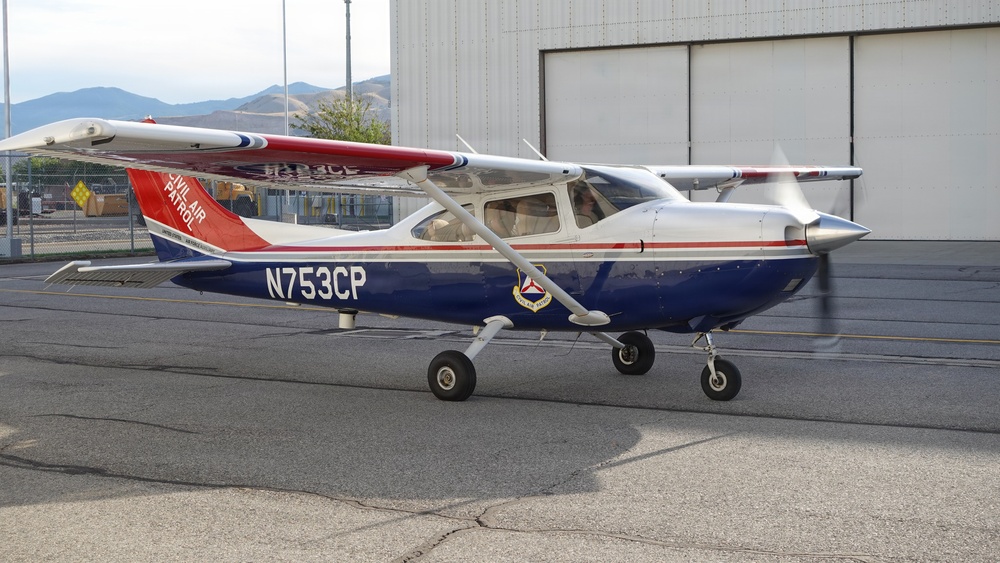 A Civil Air Patrol Cessna aircraft with tail number N753CP is parked on a tarmac in front of a hangar. The aircraft is painted in the distinctive Civil Air Patrol livery of blue, white, and red with the organization's shield emblem visible on the fuselage. The propeller appears to be spinning, suggesting the engine is running.