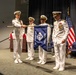 A formal U.S. Navy change of command ceremony is taking place on a stage, with officers in dress white uniforms participating in the transfer of a unit guidon. The pennant visible reads 'OICC PSNS Bremerton, WA,' indicating this is the Officer in Charge of Construction, Puget Sound Naval Shipyard, located in Bremerton, Washington. Four naval officers are centrally involved in the ceremony, with an American flag and a U.S. Navy flag visible in the background.