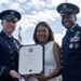 Two military officers in dress uniforms are presenting a Certificate of Appreciation to a civilian woman at what appears to be an official military ceremony. The certificate is made out to 'Analida Simmons' and is dated February 2022. All three individuals are smiling and posing for the photograph outdoors.
