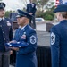 A formal U.S. Air Force military ceremony is taking place outdoors, likely a retirement or change of command ceremony. A senior non-commissioned officer in the center is holding a folded American flag, preparing to present it to a female Chief Master Sergeant facing him. Multiple uniformed personnel with service dress blues and various rank insignia are present on and near a stage.