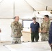 A group of U.S. Army personnel and at least one civilian are gathered inside a military command tent for what appears to be a briefing or planning session. They are standing around a table with maps spread out, suggesting operational or tactical planning activity. The setting is a standard military field tent with beige canvas walls and portable lighting.