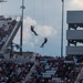Two individuals in military-style gear are rappelling or fast-roping from ropes suspended high above a large stadium filled with spectators. The demonstration appears to be a pre-event or halftime military exhibition performed for a large crowd. The stadium structure, lighting towers, and multi-level press/luxury boxes are visible in the background.