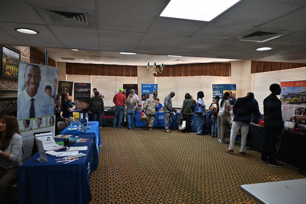 The image shows an indoor job fair or career expo taking place in a banquet or conference room. Multiple employer booths are set up along the walls and in rows, with attendees browsing and speaking with representatives. Visible organizations include Clune Construction, Gemfire, and a DFW-branded booth, among others.