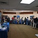 The image shows an indoor job fair or career expo taking place in a banquet or conference room. Multiple employer booths are set up along the walls and in rows, with attendees browsing and speaking with representatives. Visible organizations include Clune Construction, Gemfire, and a DFW-branded booth, among others.