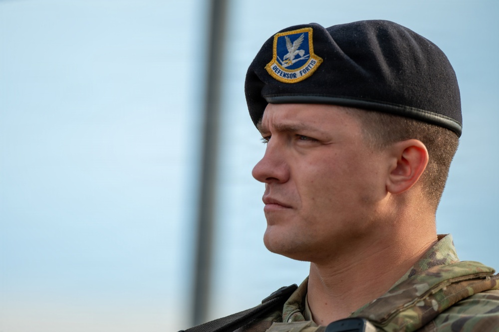 A close-up portrait of a male military service member wearing a black beret with a 'Defensor Fortis' insignia badge, indicating affiliation with the United States Air Force Security Forces. He is dressed in a multicam/OCP camouflage uniform and appears to be at attention or standing in a formal posture. The image is a sharp, professional-quality photograph with a blurred background.