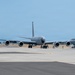 The image shows U.S. Air Force military aircraft taxiing on a flight line at what appears to be a military airbase. The primary aircraft in the foreground is a large gray jet, consistent with a KC-135 Stratotanker aerial refueling aircraft, viewed from the front. A second aircraft marked 'U.S. AIR FORCE' is visible to the right, along with ground support vehicles in the background.