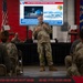 A military officer in camouflage uniform is delivering a briefing or presentation to an audience of seated military personnel in what appears to be a hangar or large facility. The presentation slide behind him is titled 'Joint Integration: Stronger Together' and references the 321st Contingency Response Squadron conducting a Humanitarian Aid/Disaster Response operation in Venezuela, July 2026. An American flag and what appears to be a unit flag are visible flanking the presentation screen.