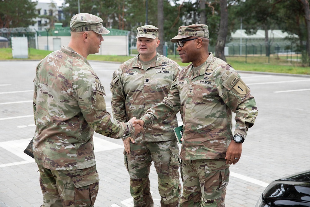 Three U.S. Army soldiers in OCP (Operational Camouflage Pattern) uniforms are engaged in a meeting or greeting in what appears to be a military installation parking area. Two of the soldiers are shaking hands while a third stands between them. Name tapes visible on two soldiers read 'CUTLER' and 'ROME', with 'U.S. ARMY' tape visible on both.