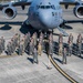 A large group of U.S. Air Force personnel pose for a formal group photograph in front of a C-17 Globemaster III military transport aircraft on a flight line tarmac. The aircraft bears the tail number 0103 and markings for the 62nd AW and 446th AW, indicating Joint Base Lewis-McChord (JBLM) in Washington State. Personnel are wearing a mix of flight suits and Army Combat Uniforms (ACU/OCP), suggesting a joint or mixed-unit gathering.
