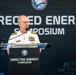 A senior U.S. Navy officer in white dress uniform is speaking at a podium during the Directed Energy Symposium. The officer displays multiple ribbons and rank insignia consistent with flag officer grade. The event appears to be a formal military-academic or defense industry conference.