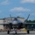The F-35A Lightning II offically arrives at the 104th Fighter Wing, brings new era to Barnes Air National Guard Base A Lockheed Martin F-35 Lightning II stealth fighter jet is taxiing on a runway apron during what appears to be a military air show. The aircraft is viewed head-on with its landing gear deployed, and a pilot is visible in the cockpit. A large crowd of spectators, including uniformed military personnel and civilians, lines the tarmac in the background.