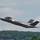 The F-35A Lightning II offically arrives at the 104th Fighter Wing, brings new era to Barnes Air National Guard Base A single-seat stealth fighter jet, identifiable as an F-35A Lightning II, is captured in low-altitude flight just after takeoff or during a low pass. The aircraft bears tail markings including the letters 'WI' and a partial serial number visible on the vertical stabilizer, suggesting Wisconsin Air National Guard affiliation. The background features a dense treeline and partly cloudy sky.