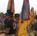 A U.S. Army military formation ceremony featuring soldiers in physical training attire and campaign hats carrying unit guidons and colors adorned with numerous campaign and award streamers. The prominent yellow flags with gold fringe are consistent with U.S. Army cavalry unit colors. The event appears to be a formal regimental or brigade-level ceremony, likely at a U.S. Army installation.