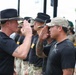 A military ceremony is taking place outdoors where personnel in black PT (physical training) shirts and military camouflage pants are raising their right hands, likely taking an oath or being sworn in. A senior figure wearing a black cavalry-style Stetson hat is administering the ceremony to a line of soldiers. The event appears to be a formal military reenlistment or induction ceremony conducted in an open-air setting.