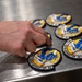 A hand is arranging multiple embroidered military patches on a stainless steel surface. The patches belong to the '18th Fighter Interceptor Squadron' and feature a blue eagle or bird design on a yellow and white background with a black border. Multiple identical patches are visible, suggesting inventory management or distribution activity.