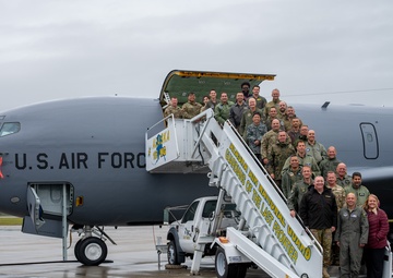 A large group of U.S. Air Force personnel and civilians pose for a group photo on and around a mobile staircase positioned at the door of a U.S. Air Force aircraft, tail number 8876. The aircraft bears the markings of the 168th Wing and the inscription 'Alaska Air National Guard - Guardians of the Last Frontier.' The wet tarmac and overcast sky suggest the photo was taken in Alaska, consistent with the unit's known base at Eielson or Fairbanks.