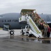 A large group of U.S. Air Force personnel and civilians pose for a group photo on and around a mobile staircase positioned at the door of a U.S. Air Force aircraft, tail number 8876. The aircraft bears the markings of the 168th Wing and the inscription 'Alaska Air National Guard - Guardians of the Last Frontier.' The wet tarmac and overcast sky suggest the photo was taken in Alaska, consistent with the unit's known base at Eielson or Fairbanks.