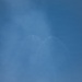 The image shows a blue sky with thin, wispy cloud formations or contrails forming a V-shape or wing-like pattern near the center of the frame. Two small bright points are visible at the apex of the V-shape, possibly aircraft or light reflections. The overall image is hazy and low in contrast.