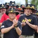A group of U.S. Army soldiers wearing black cavalry Stetson hats with gold crossed-sabers insignia are gathered at what appears to be a military ceremony or event. The soldiers are dressed in black Army PT (physical training) shirts and are clapping or applauding. The central figure wears a hat with a Command Sergeant Major insignia, indicating senior enlisted rank.