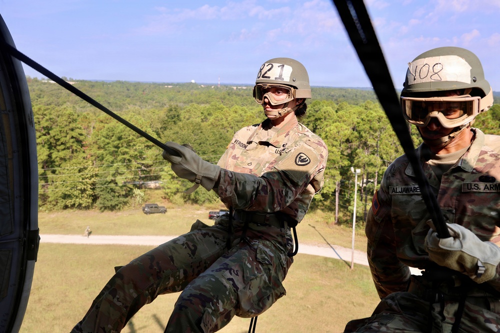 Two U.S. Army soldiers are conducting a rappelling exercise from what appears to be a helicopter or elevated platform. The soldier in the foreground, wearing helmet number 321 with the last name 'VERDONE' visible, is actively rappelling while gripping a rope. A second soldier with helmet number 408 and name tag 'ALJAWARE' observes from inside the aircraft.