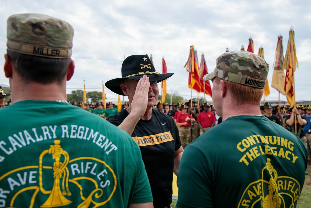 A military ceremony involving members of the 3rd Cavalry Regiment ('Brave Rifles') is taking place outdoors. A senior officer wearing a black cavalry Stetson hat with a general's star insignia and a 'First Team' shirt appears to be saluting or greeting two soldiers named Miller and Morrison, who are wearing green 'Brave Rifles - Continuing the Legacy' shirts. A large formation of troops carrying unit guidons and flags is visible in the background.