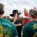 A military ceremony involving members of the 3rd Cavalry Regiment ('Brave Rifles') is taking place outdoors. A senior officer wearing a black cavalry Stetson hat with a general's star insignia and a 'First Team' shirt appears to be saluting or greeting two soldiers named Miller and Morrison, who are wearing green 'Brave Rifles - Continuing the Legacy' shirts. A large formation of troops carrying unit guidons and flags is visible in the background.