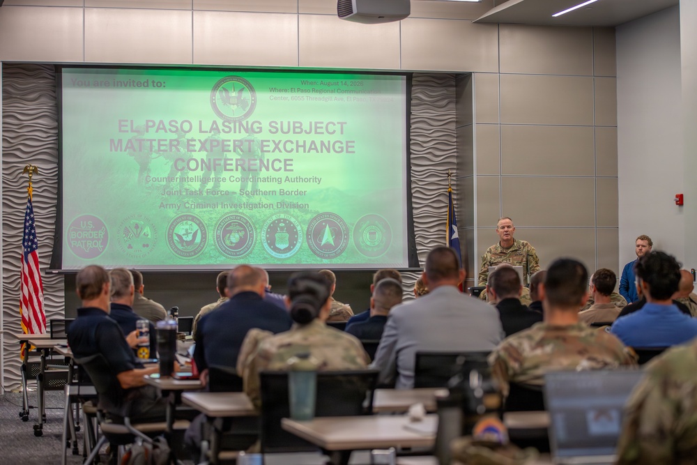 A military and law enforcement conference is taking place in a modern conference room. The presentation screen displays 'El Paso LASING Subject Matter Expert Exchange Conference' organized by Counterintelligence Coordinating Authority, Joint Task Force – Southern Border, and Army Criminal Investigation Division. An officer in military camouflage uniform is speaking at a podium to an audience of mixed military and civilian attendees.