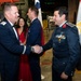 Two military officers in dress uniforms are shaking hands at what appears to be a formal military reception or gala event. One officer wears a US Air Force dress uniform while the other wears a darker uniform with numerous medals and insignia, standing near an Egyptian flag. Multiple national flags are displayed in the background, suggesting an international military gathering.