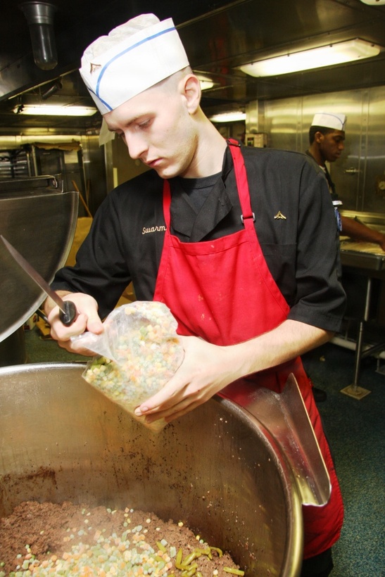 A 24th Marine Expeditionary Unit food service specialist, adds in a bag of frozen vegtables to a batch of sheppard's pie, which he is preparing for the Marines and Sailors aboard USS Mesa Verde April 5. This was the one of the meal choices provided to the troops aboard USS Mesa Verde along with a few others to chose from. At the beginning of the day, the food service specialists are given a meal to prepare, one for lunch and one for dinner. These meals are served to hundreds of Marines and Sailors so the job isn't as easy as it may be at home in your kitchen. This is the Marines and Sailors third month of deployment and the meals keep coming. These Marines and Sailors take pride in what they cook day after day and never let their personal hardships interfere with the job.